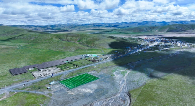 Vue a&eacute;rienne d'un micro-r&eacute;seau photovolta&iuml;que &agrave; c&ocirc;t&eacute; d'un village isol&eacute; de haute altitude, entour&eacute; de prairies et de montagnes