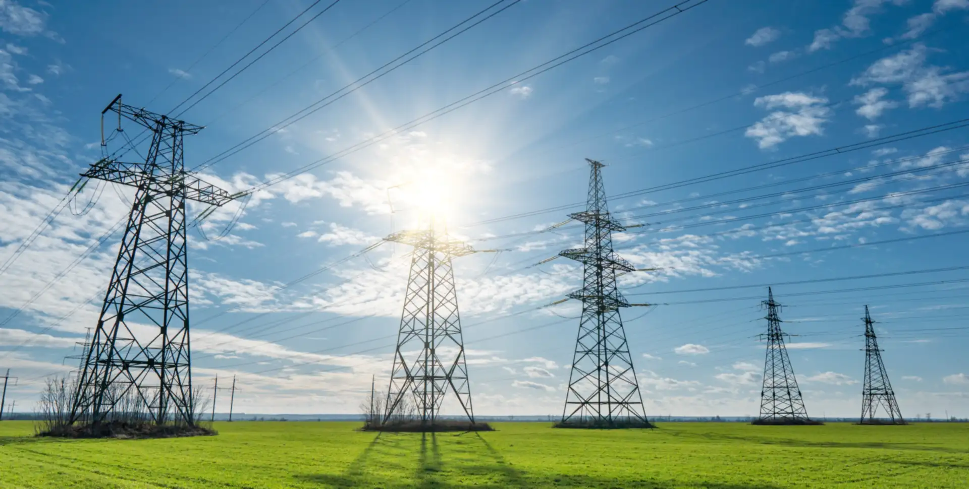 Pyl&ocirc;nes de transport d'&eacute;lectricit&eacute; &agrave; travers des champs verdoyants sous un soleil &eacute;clatant